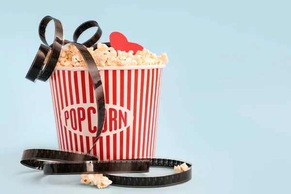 Bucket of popcorn with film reel and paper heart on blue background. Valentine\'s Day celebration
