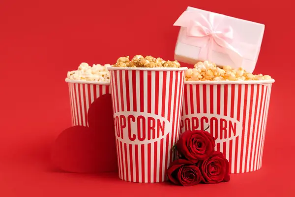 Buckets of popcorn with gift box and beautiful roses on red background. Valentine\'s Day celebration
