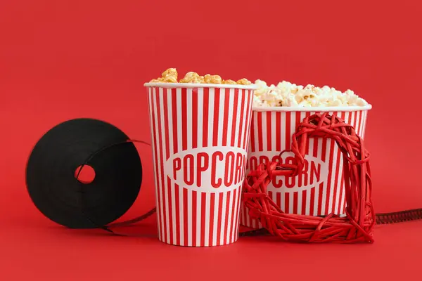 Buckets of popcorn with film reel and decorative heart on red background. Valentine\'s Day celebration