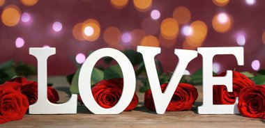 Kırmızı güller ve aşk kelimesi arka planda bulanık ışıklarla. Sevgililer Günü kutlaması