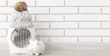 Elektrikli radyatör örgü şapkalı ve kumbarası beyaz tuğla duvarın yanında. Tasarım için pankart