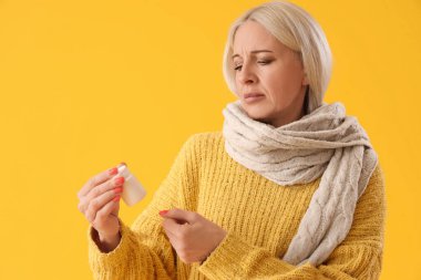 Sarı arka planda ilaç şişesi olan olgun bir kadın.