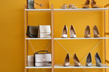 Raflarda şık kadın ayakkabıları ve turuncu duvarın yanında farklı çantalar var.