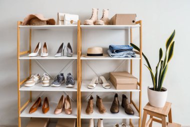 Değişik kadın ayakkabılarına, kıyafetlerine ve çiçeklerine sahip raf ünitesi butikte ışık duvarının yanında.