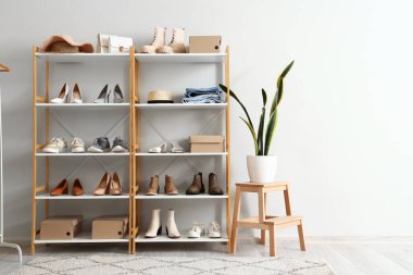 Değişik kadın ayakkabılarına, kıyafetlerine ve çiçeklerine sahip raf ünitesi butikte ışık duvarının yanında.