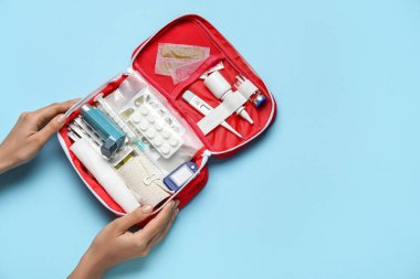 İlk yardım çantası ve mavi arka planda hapları olan kadın eller.
