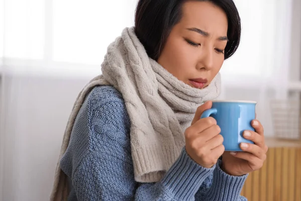 Ill Asian woman with cup of tea at home, closeup