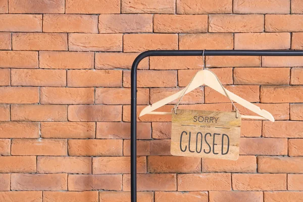 Wooden sign with text WE'RE CLOSED hanging on rack near brick wall