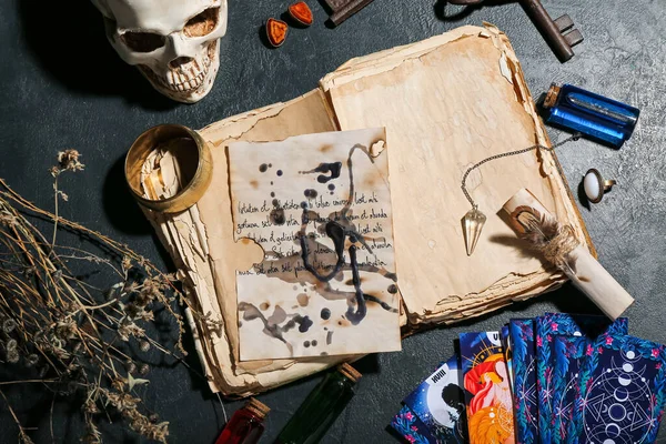 Witch's magic attributes with book and tarot cards on dark table