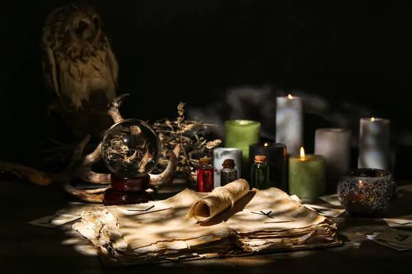 Witch\'s magic attributes with book, owl, crystal ball of fortune teller and candles on dark table
