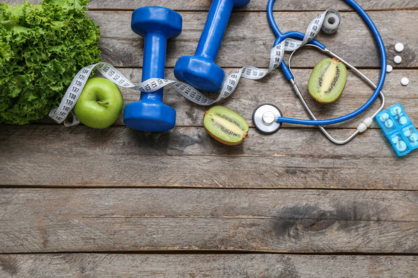 Composition with dumbbells, stethoscope, pills and healthy food on wooden background