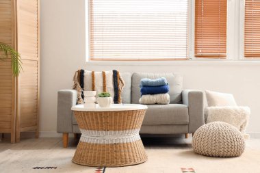 Gri kanepe ve sehpanın üzerinde bir yığın kıyafetle oturma odasının içinde.