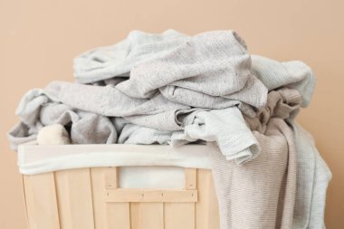 Kirli elbiseli çamaşır sepeti bej duvarın yanında, yakın plan.