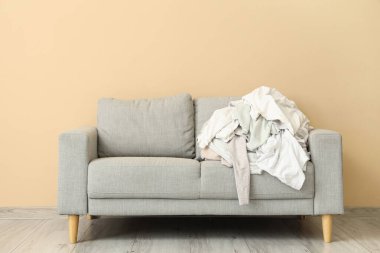 Bej duvarın yanında kirli giysi yığını olan gri kanepe.