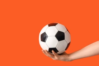 Turuncu arka planda futbol topu olan bir kadın el.