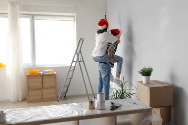Noel Baba şapkalı genç çift yeni evlerinin tamiri sırasında duvar boyuyor.