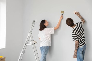 Boya fırçası ve malası olan genç bir çift yeni evlerinde tamir yapıyor.