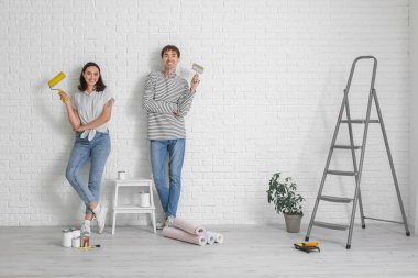 Yeni evlerinde tamirat sırasında boya silindirli ve fırçalı genç bir çift.