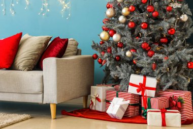 Noel ağacının altında farklı hediye kutuları ve renk duvarına karşı kanepe.