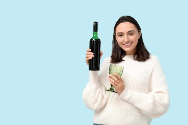 Mavi arka planda cam ve kırmızı şarap şişesi olan güzel genç bir kadın.