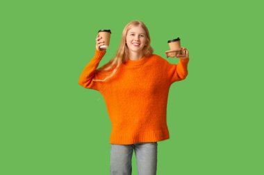 Yeşil arka planda çay fincanları olan güzel, genç ve mutlu bir kadın.