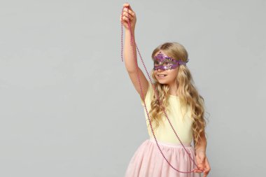 Hafif arka planda karnaval maskesi takan sevimli küçük kız.