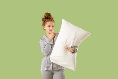 Yeşil arka planda beyaz yumuşak yastıklı düşünceli genç bir kadın.