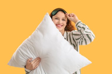 Turuncu arka planda beyaz yumuşak yastıklı, uyku maskeli mutlu genç kadın.