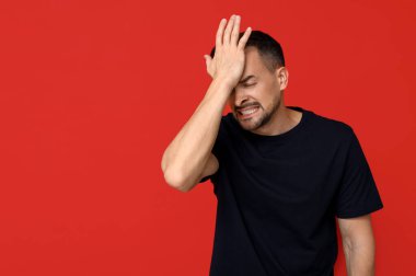 Yakışıklı, utangaç, yüzü kırmızı arka planda genç bir adam.