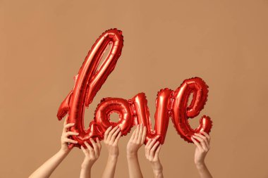 Kahverengi arka planda aşk kelimesi şeklinde balonları olan kadın elleri. Sevgililer Günü kutlaması