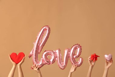 Aşk kelimesi şeklinde balonları olan kadın elleri, kahverengi arka planda hediye kutusu ve kumaş kalp. Sevgililer Günü kutlaması