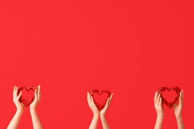 Kırmızı arka planda dekoratif kalpleri olan kadın elleri. Sevgililer Günü kutlaması
