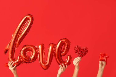 Kelime şeklinde balonları olan kadın eller. Aşk, dekoratif kalp ve kırmızı arka planda hediye kutusu. Sevgililer Günü kutlaması