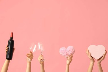 Kumaş kalpli, gözlüklü, şarap şişeli ve pembe arka planda hediye kutusu olan kadın elleri. Sevgililer Günü kutlaması