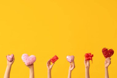 Farklı kalpleri olan kadın elleri ve sarı arka planda hediye kutuları. Sevgililer Günü kutlaması