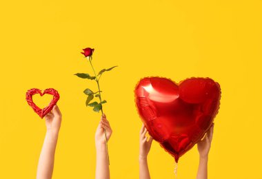 Kalp şeklinde hava balonu ve sarı arka planda kırmızı gül olan kadın elleri. Sevgililer Günü kutlaması