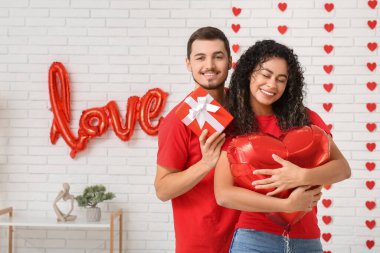 Evde sevgililer günü için kalp şeklinde balonları ve hediyeleri olan genç bir çift.