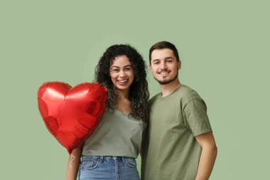 Yeşil arka planda Sevgililer Günü için kalp şeklinde balonu olan genç bir çift.