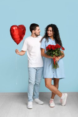 Sevgililer günü için mavi duvarın yanında kalp şeklinde balonları ve gül çiçekleri olan genç bir çift.