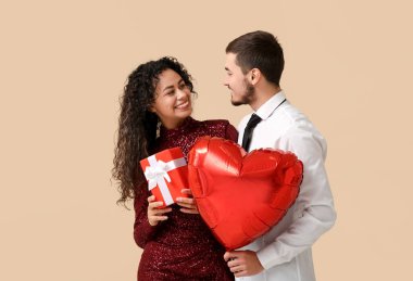 Kalp şeklinde hava balonu olan genç bir çift ve bej arka planda Sevgililer Günü hediyesi.