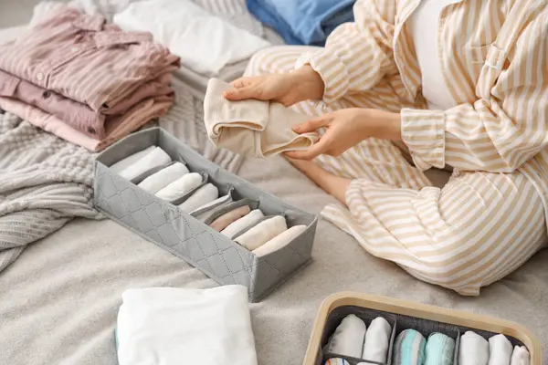 Woman sorting clothes on bed in bedroom, closeup