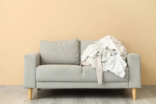 Grey sofa with pile of dirty clothes near beige wall