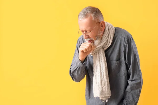 Sick mature man in scarf sneezing on yellow background