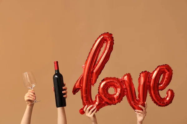 Female hands with air balloons in shape of word LOVE and bottle of wine on brown background. Valentine\'s Day celebration