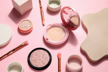 Makyaj fırçaları ve pembe arka planda podyumlarla dekoratif kozmetik ürünler.