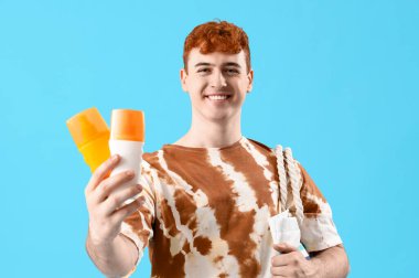 Mavi arka planda güneş kremi şişeleri olan genç bir adam.