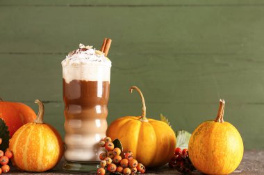 Yeşil duvarın yanındaki masada bir bardak tarçınlı ve bademli balkabaklı latte.