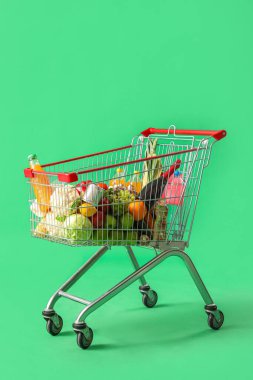 Yeşil arka planda farklı yiyeceklerle dolu alışveriş arabası.