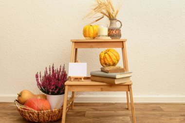 Beyaz duvarın yanında balkabağı, kitap ve kenevir çiçekli tahta merdiven.