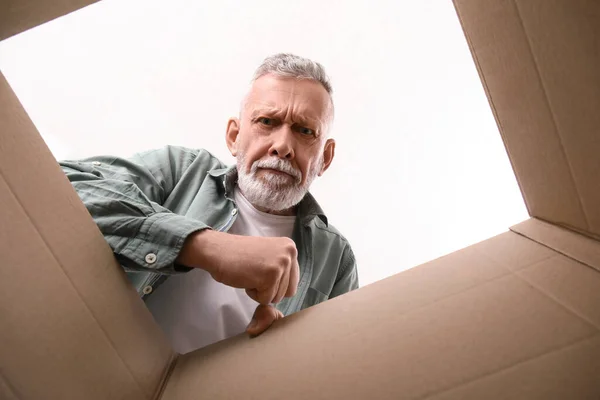 Angry mature man with open parcel at home, view from inside